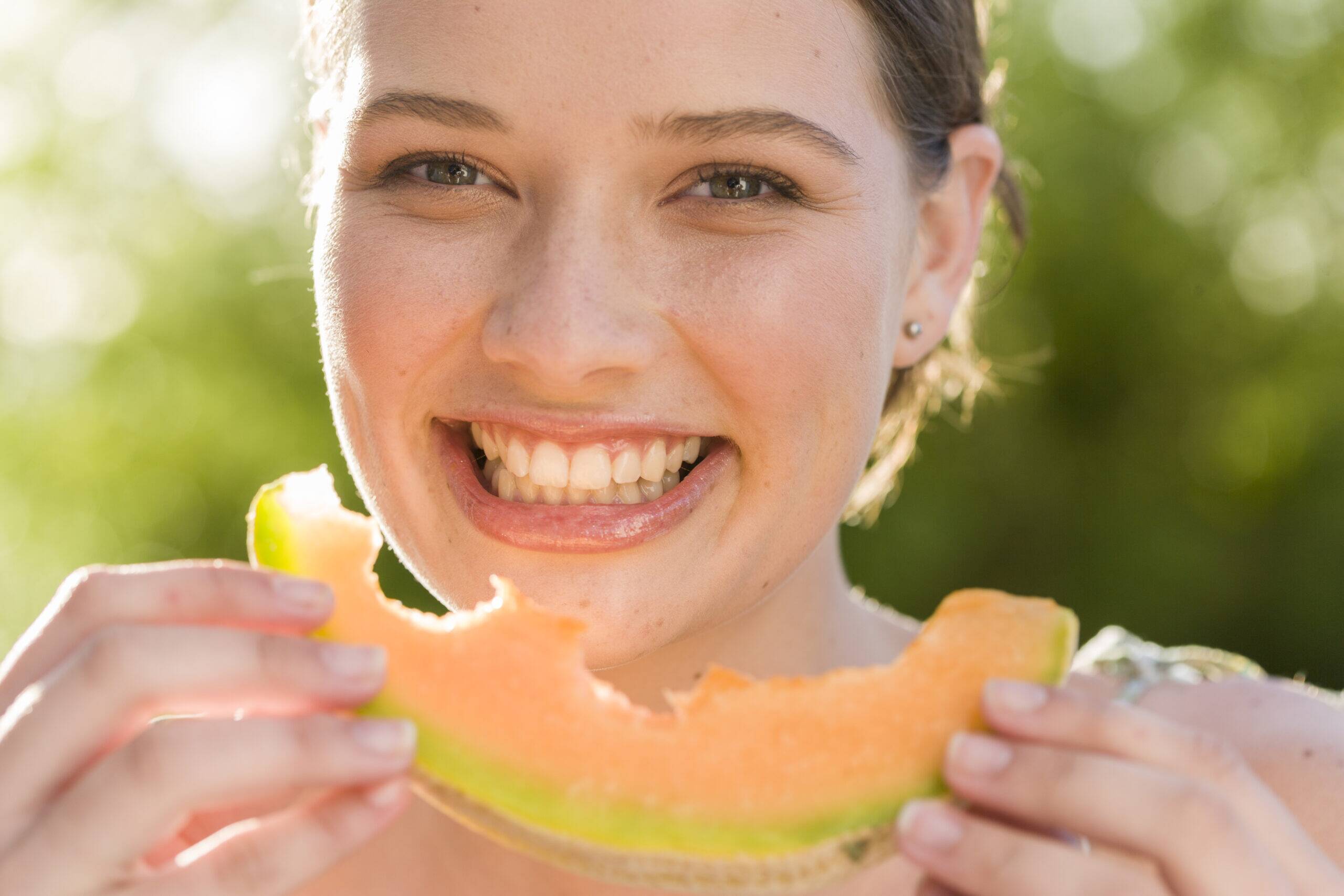portrait-smiling-woman-eating-melon-outdoors