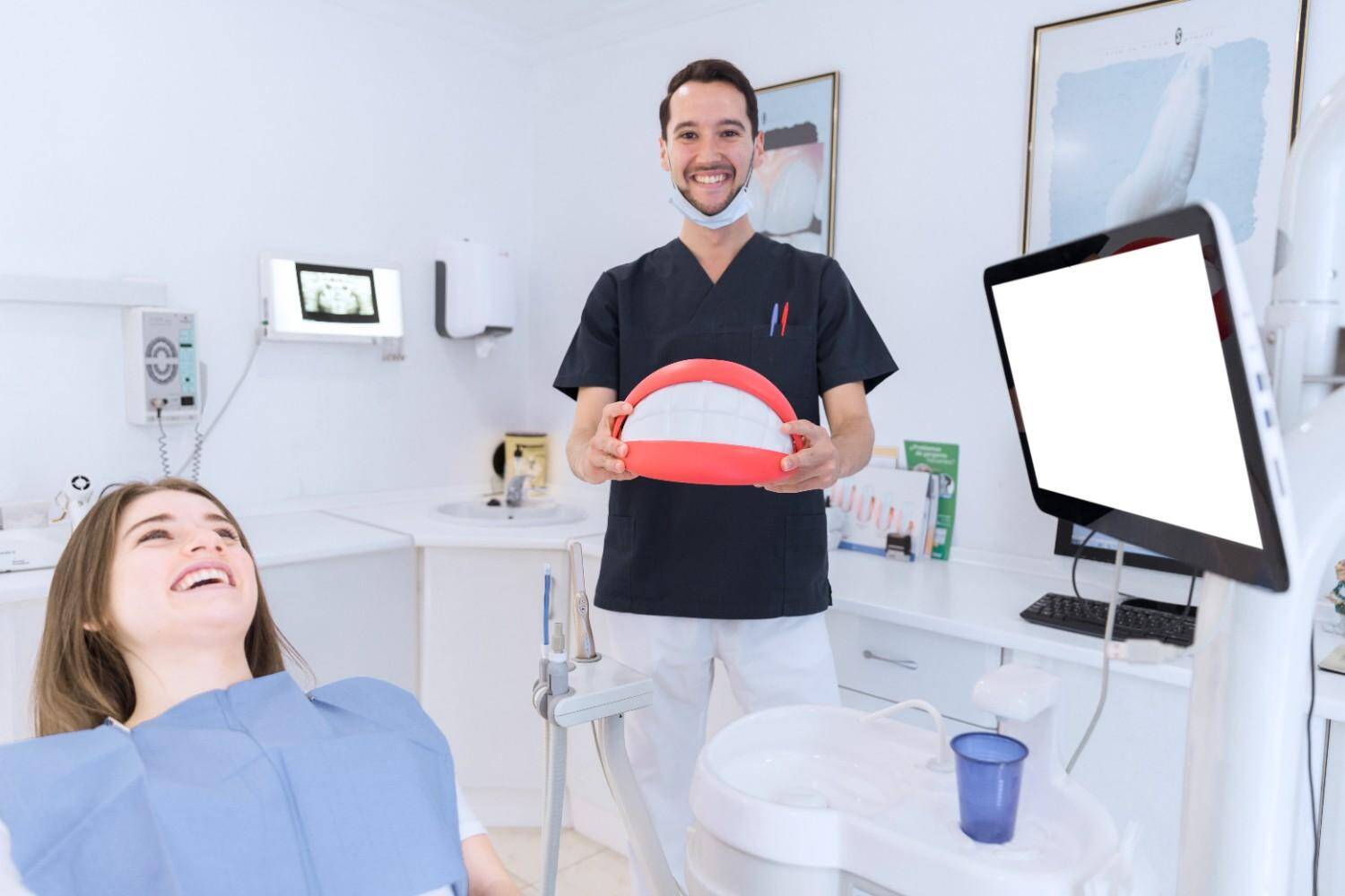 Happy male dentist holding a large teeth model in a clinic