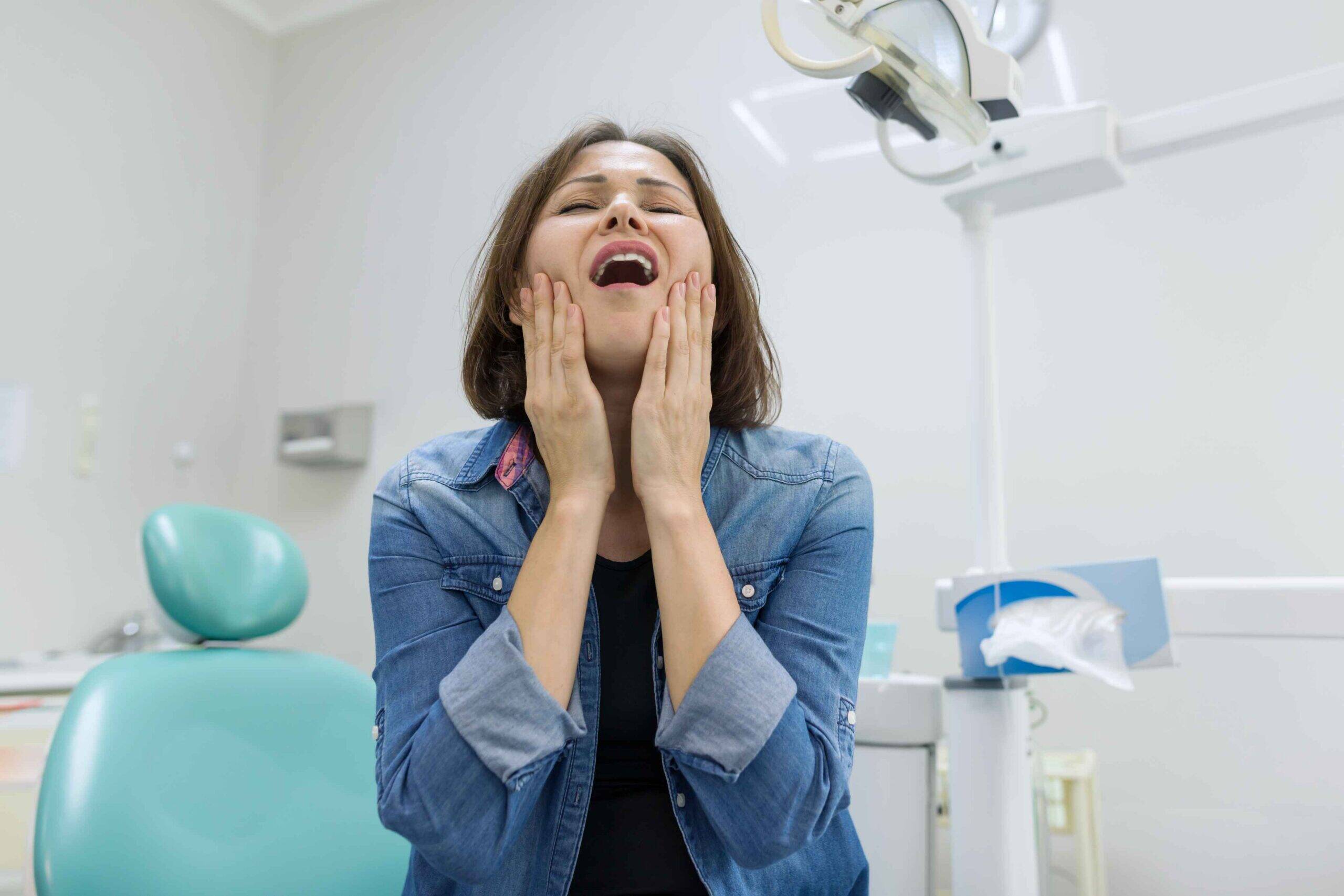 Woman holding her jaw with severe tooth pain in a dental clinic.